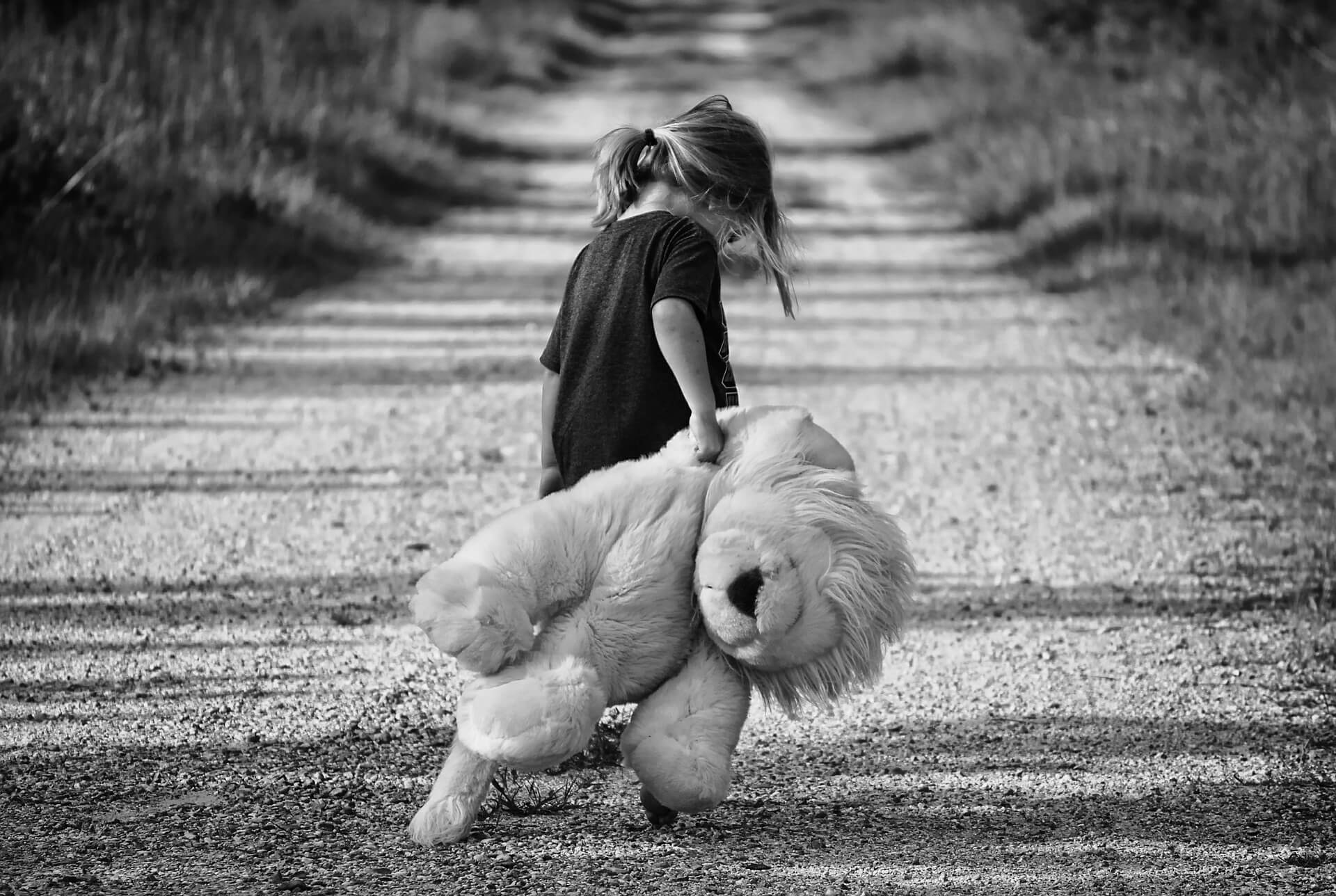 Une petite fille avec sa peluche sur un chemin. 