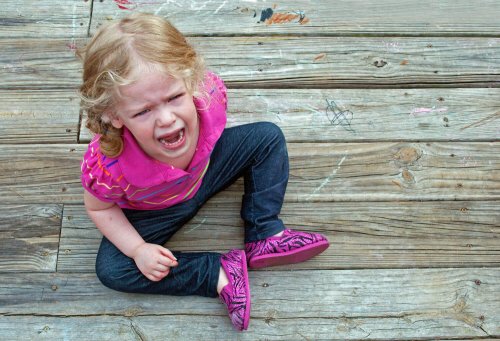 Niña de dos años sentada en el suelo llorando por una rabieta.