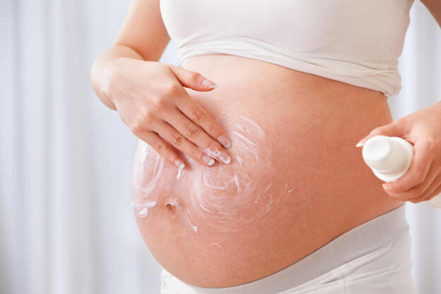 mulher grávida passando hidratante na barriga