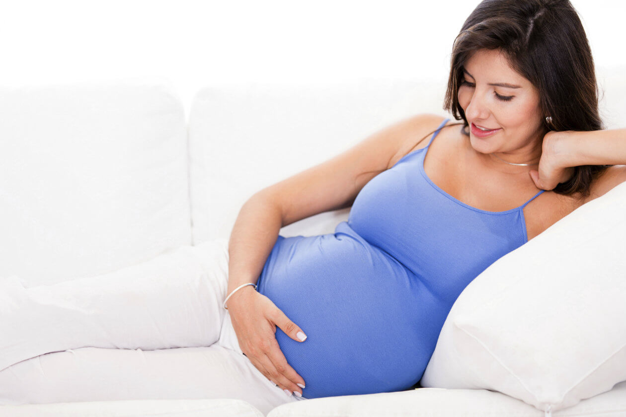 Mujer embarazada agarrando su tripa y sonriendo