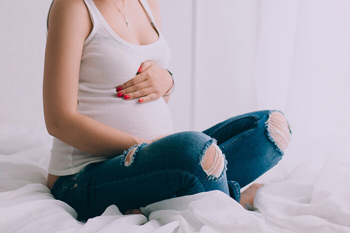 Une femme enceinte assise qui se touche le ventre dans son lit.