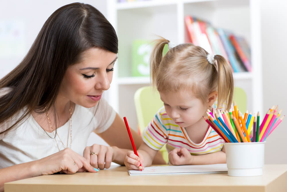 Un enfant qui dessine à côté d'un adulte.