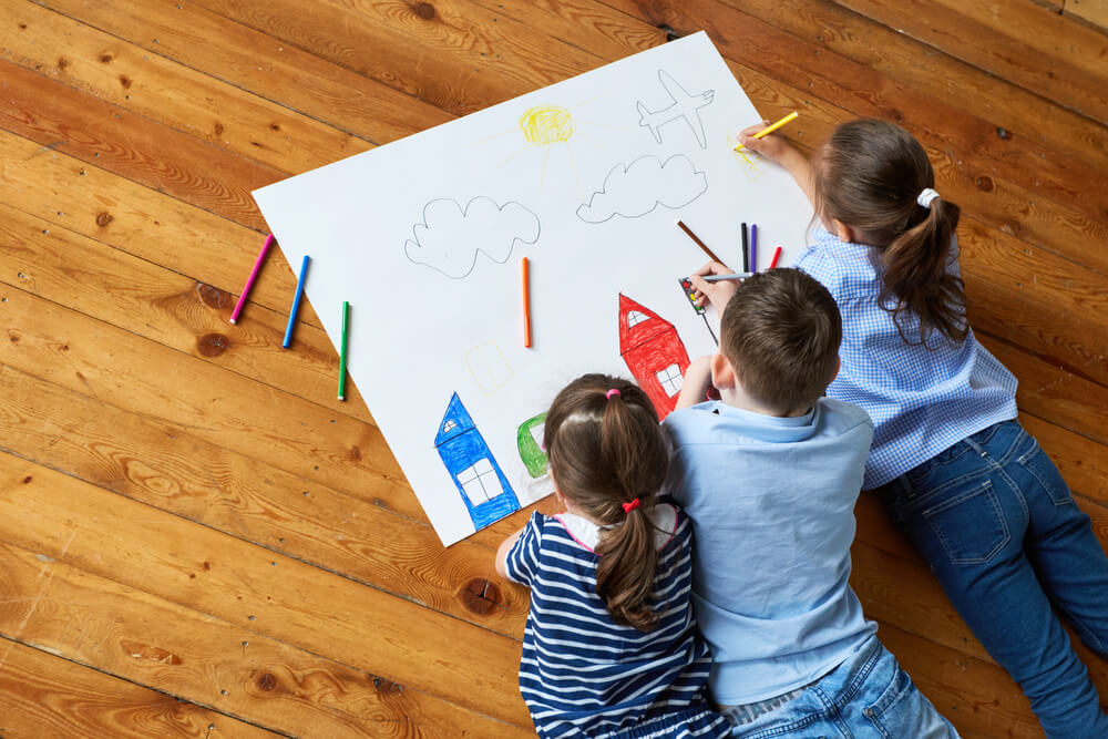 Trois enfants qui dessinent sur la même feuille.