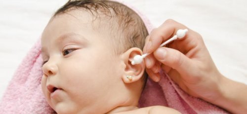 A woman cleaning a child's ear with a swab.