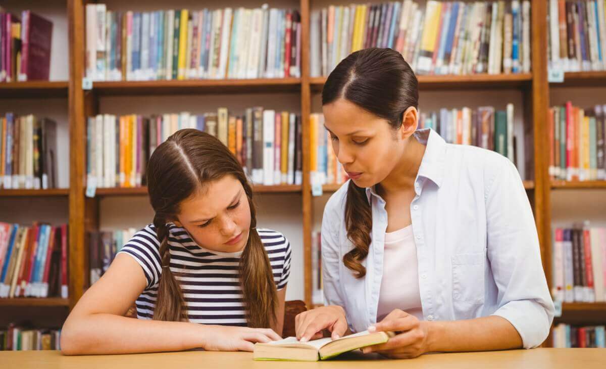 A woman and a preteen girl looking at a book in a library.