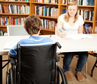 Alumno con discapacidad motora y su profesora en la biblioteca.