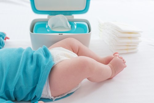 En bebis som ligger bredvid en hög med blöjor och en låda med våtservetter.