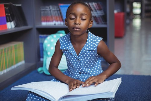 Menina lendo braille na biblioteca.