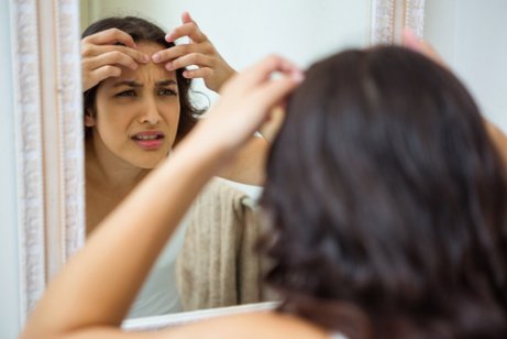 Une femme qui regarde la peau de son visage dans un miroir.