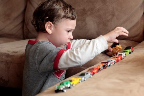Niño con autismo jugando con los coches en el sofá.