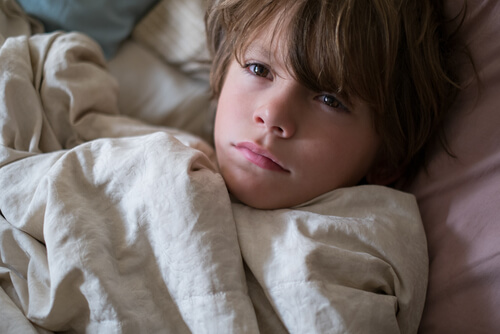 Niño arropado en la cama no puede dormir porque tiene pesadillas.