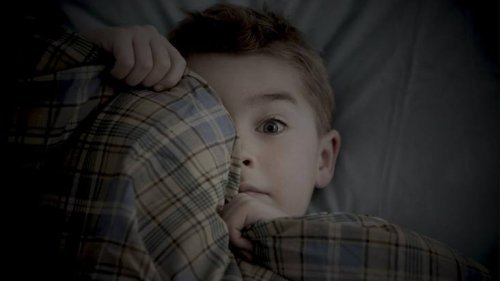 Niño en la cama tapándose la cara con la manta para ayudar a superar el miedo.