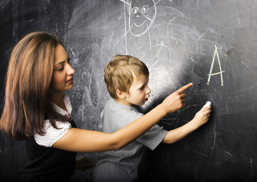 En lærer hjelper en ung gutt med å lære å skrive bokstaven A på en tavle.