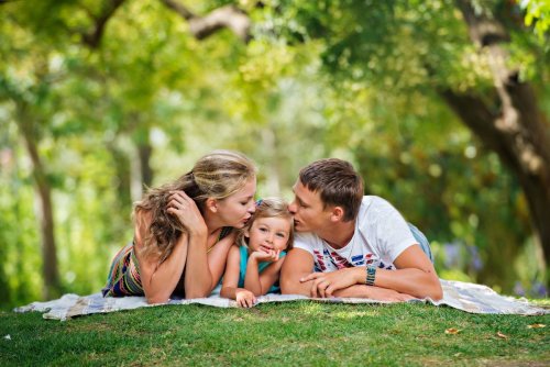 Föräldrarna ger sin dotter en puss på huvudet när de ligger på en picknickfilt i skogen.