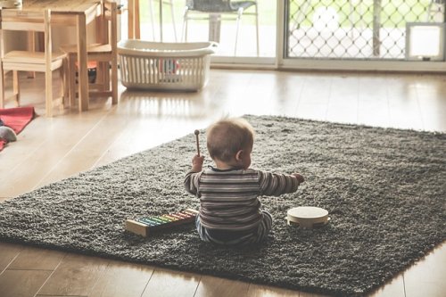Bebé sentado en una alfombra tocando un xilófono y una pandereta.