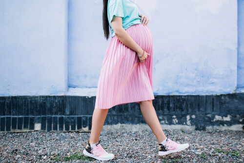 Femme enceinte marchant en jupe et baskets.