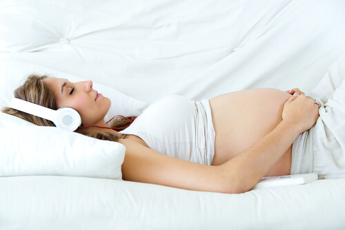 Para evitar los pensamientos negativos en el embarazo, la música siempre es una buena aliada. En este caso, la mujer está tumbada en la cama escuchando música.