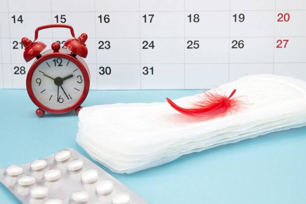 A calendar, and alarm clock, a stack of sanitary napkins, and a blister pack of pills.