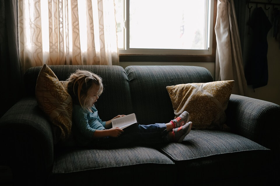 Une jeune fille qui regarder un livre sur un canapé. 