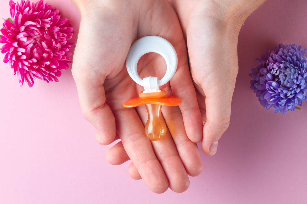 Chupón de bebé naranja con fondo roza y azul.