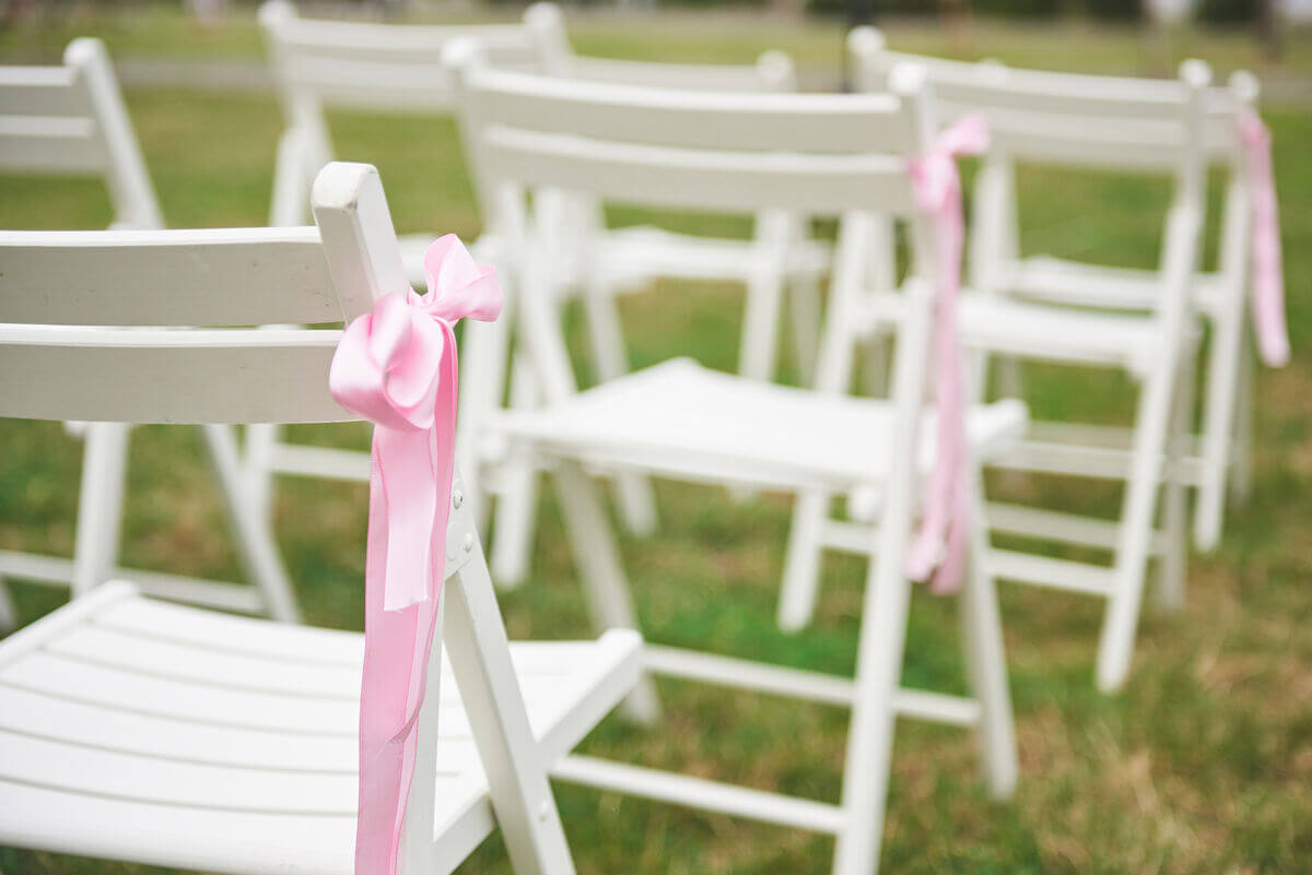 Varias sillas blancas con lazo de color rosado. 