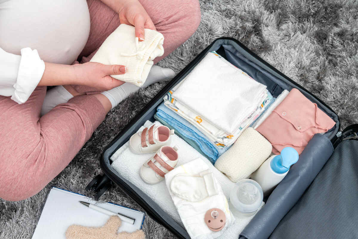 Mujer empacando ropa de bebé en una maleta.