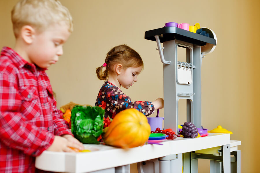 En liten gutt og en liten jente leker på et lekekjøkken.