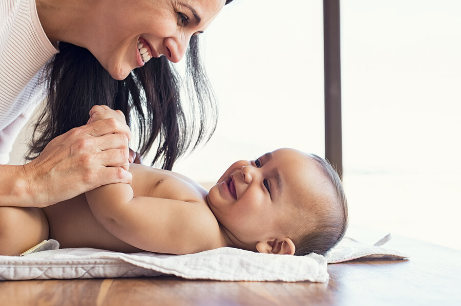 A mother playing with her giggling baby during a diaper change.