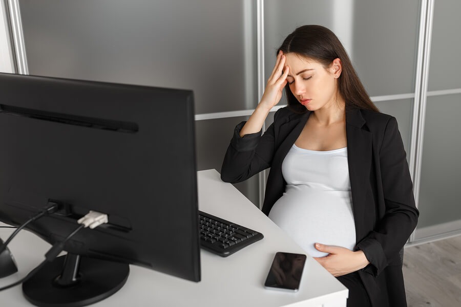 A pregnant woman sitting at her desk looking exhausted.