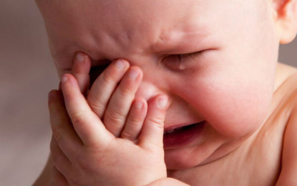 A baby covering her face with her hands while she cries.