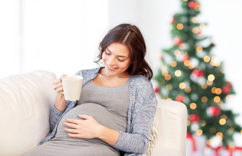 Mujer embarazada en Navidad tomando una taza de chocolate junto al árbol.