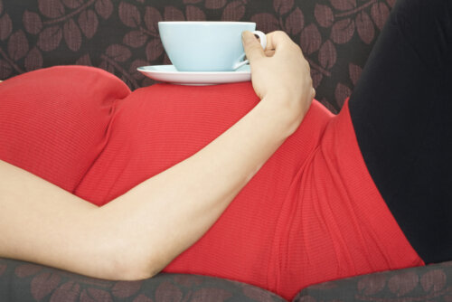 Mujer embarazada con una taza de té sobre la barriga.