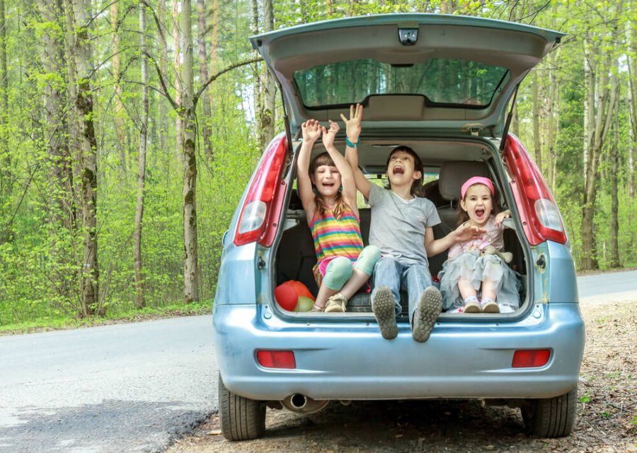 Tres niños muy contentos sentado en el maletero abierto de su coche para familias numerosas.