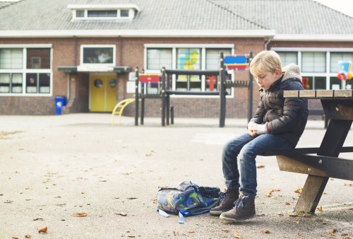 Niño sentado solo en el patio del colegio.