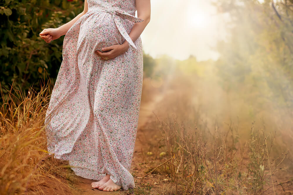 A pregnant woman wearing a floral dress walking in the country.