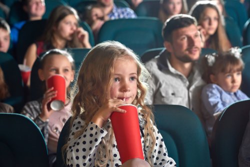 Niña bebiendo un refresco en el cine mientras ve una película.