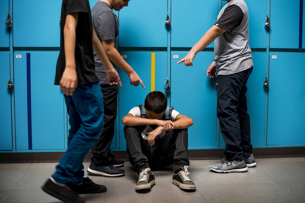 En tonåring sitter på golvet medan hans klasskamrater mobbar honom.