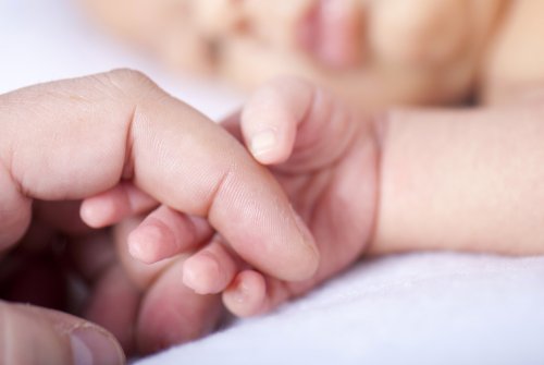 Bebé recién nacido agarrando el dedo de su madre.