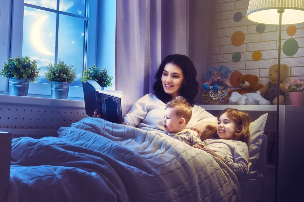 Madre leyendo un cuento a sus hijos por la noche antes de dormir.