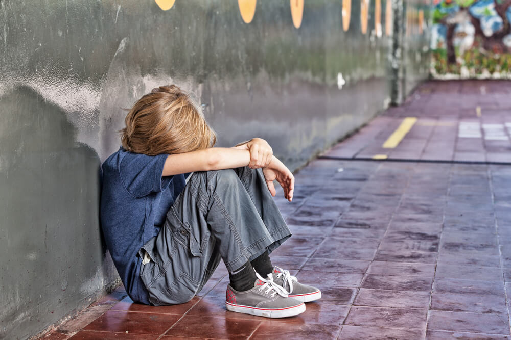 Et barn som sitter på bakken utenfor skolen og gråter.