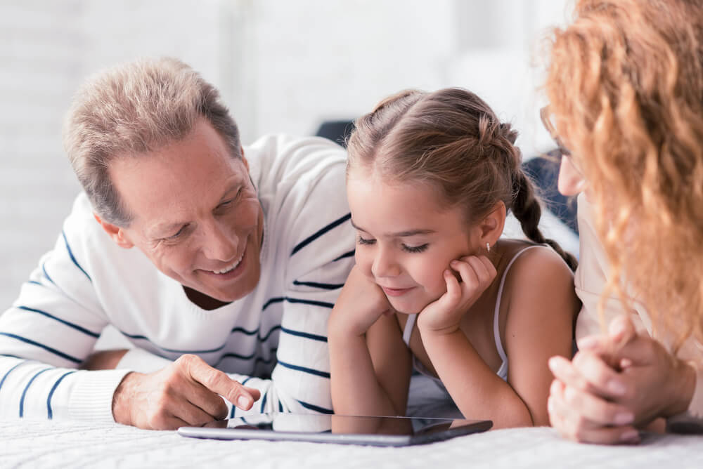 Une jeune fille qui regarde une tablette avec deux adultes.