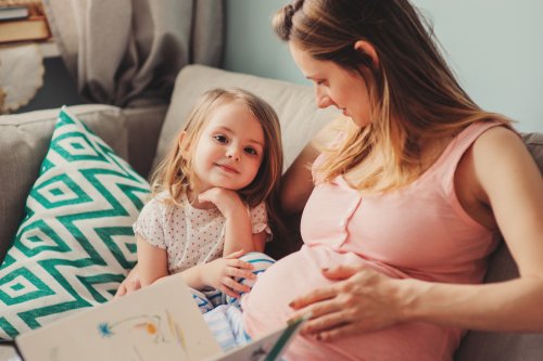 Madre embarazada con su hija leyendo libros infantiles sobre el embarazo.