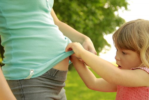 Niña curiosa mirando la barriga de su mamá embarazada.