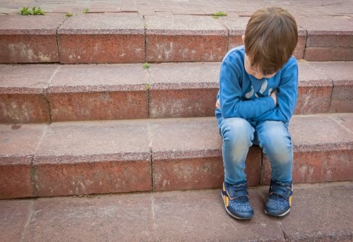 Niño que sufre acoso escolar o bullying sentado en unas escaleras solo.
