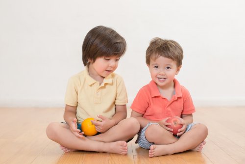 Hermanos sentados en el suelo con una fruta de la mano.