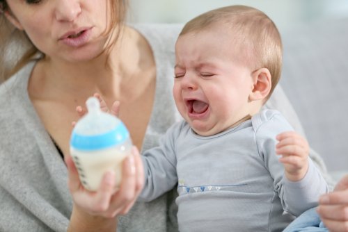 Madre intentando dar el biberón a su bebé que llora por el apego ambivalente que recibe.