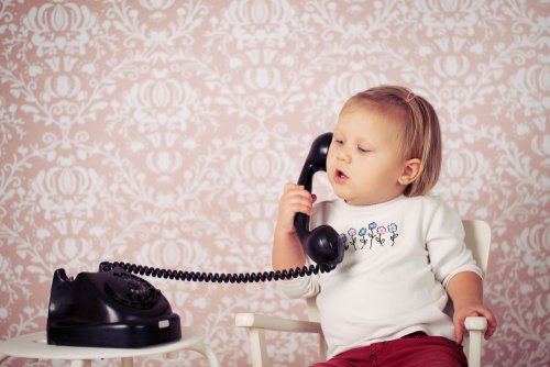 Niña bebé hablando con un teléfono antiguo para el desarrollo del lenguaje.