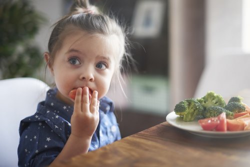 Niña comiendo en la mesa frutas y verduras.