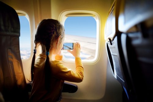 Niños haciendo una foto con el móvil por la ventanilla del avión en uno de sus vuelos de vacaciones.
