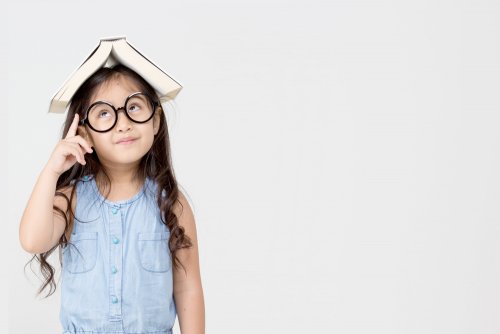 Niña con un libro en la cabeza poniendo en práctica el aprendizaje basado en el pensamiento.